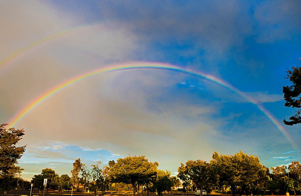 Arcobaleno in cielo blu con grande nuvola grigia