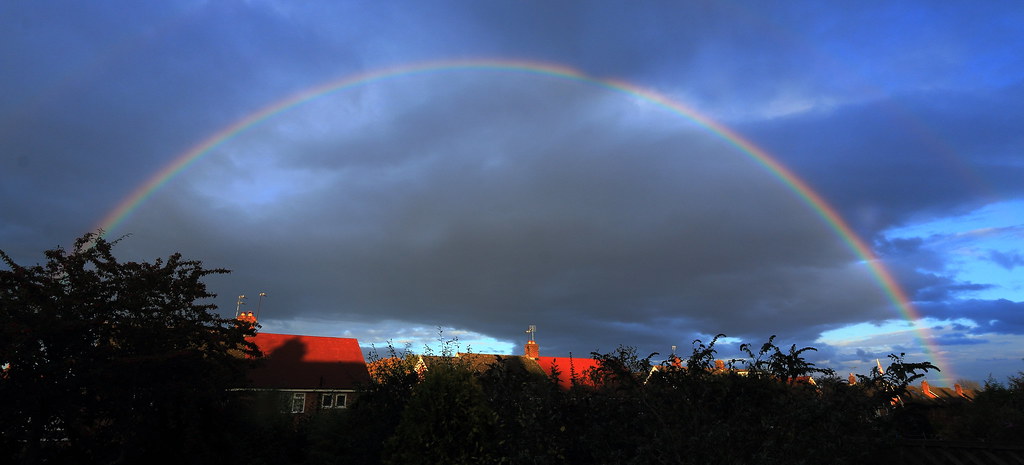 Arcobaleno in cielo blu sopra tetti di case rossi