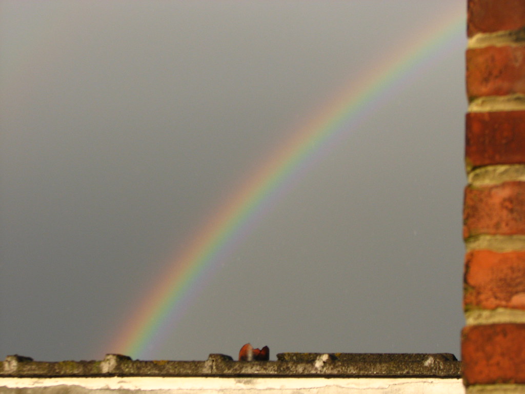 Arcobaleno in diagonale dietro muro in mattoni