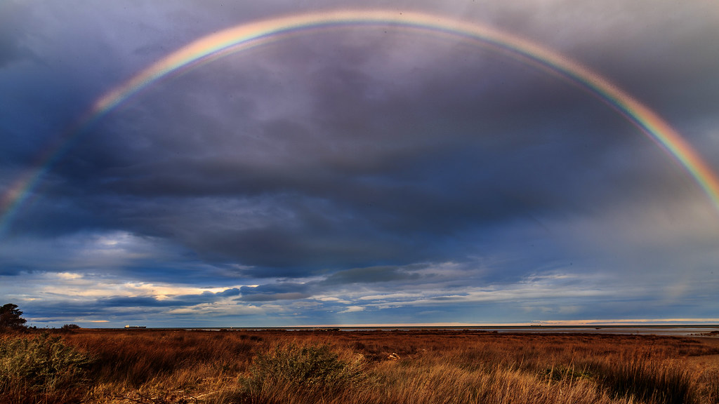 Arcobaleno leggermente interrotto in cielo nuvoloso blu