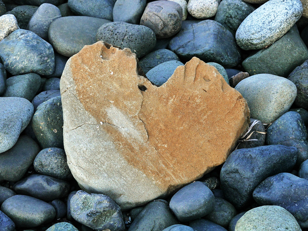 Cuore di pietra sulla spiaggia assieme a ciottoli