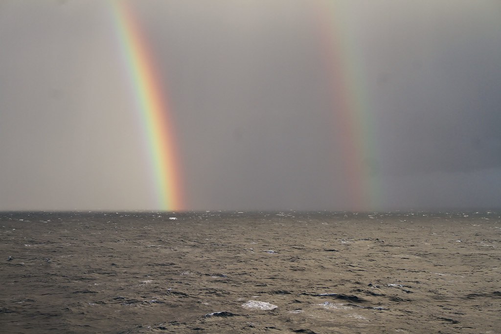 Doppio arcobaleno che si estende dal mare plumbeo