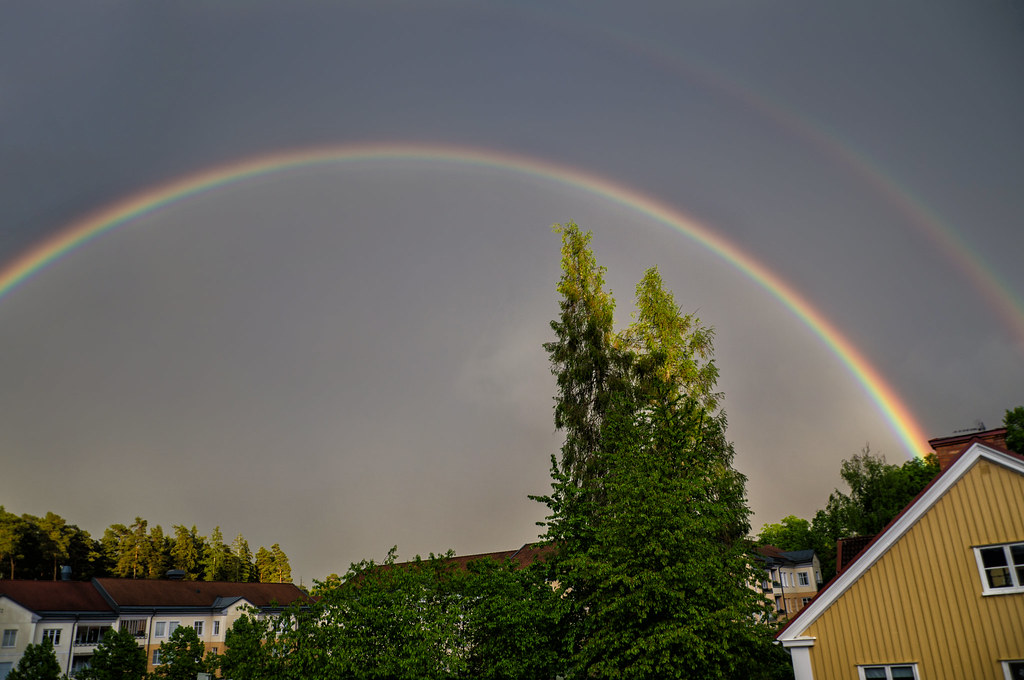 Doppio arcobaleno sopra alberi irti e tetti di case