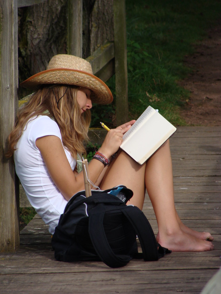 Ragazza con cappello che scrive seduta su pavimento di legno