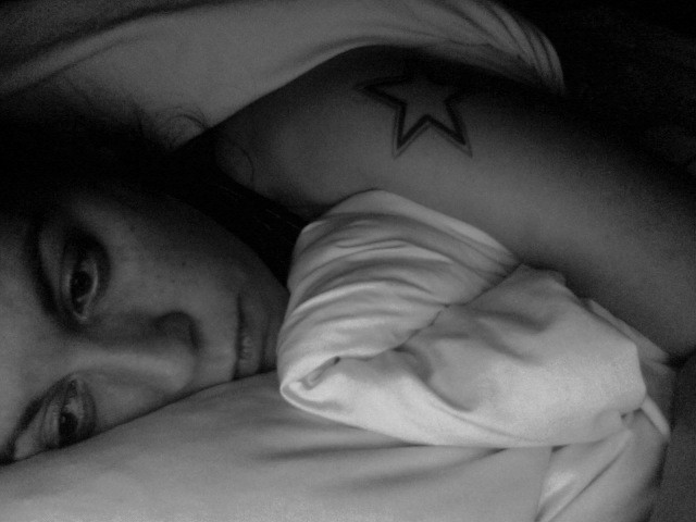 Ragazza triste con tatuaggio sulla spalla al letto in bianco e nero