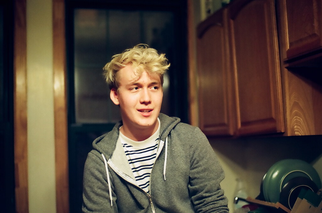 Ragazzo biondo in felpa con capelli voluminosi che sorride